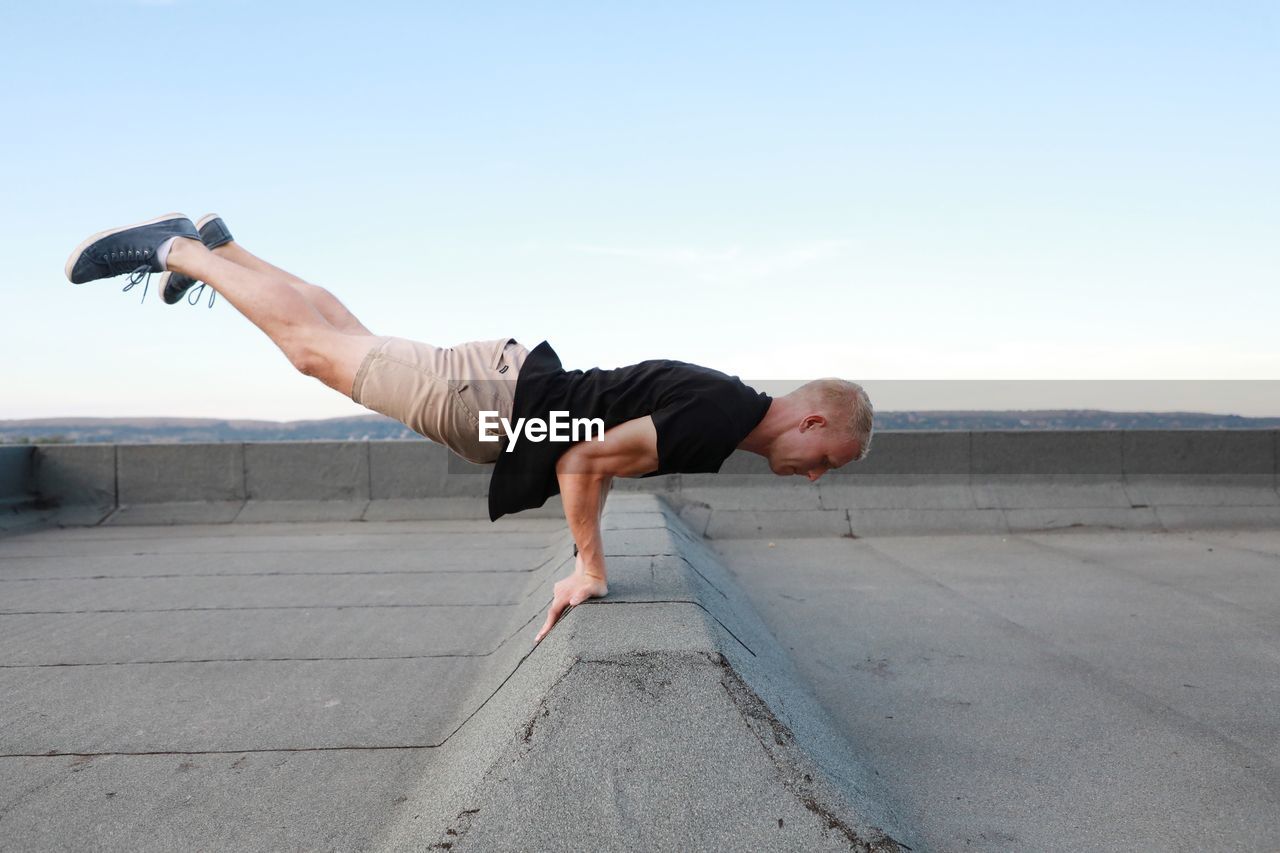 Full length of man exercising on building terrace against the sky