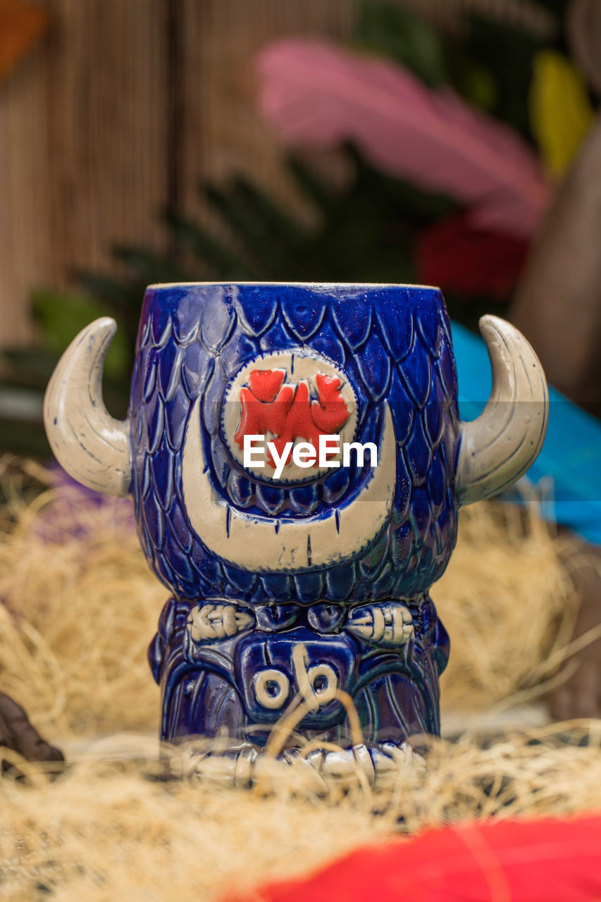 Bull shaped tiki mug of alcohol drink with froth placed against dry grass and feathers on blurred background