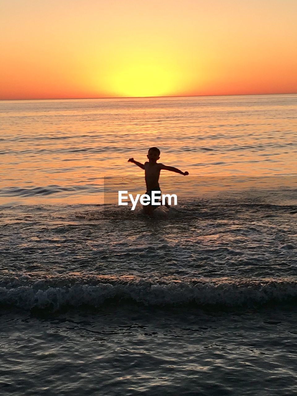 Silhouette boy jumping in sea against sky during sunset