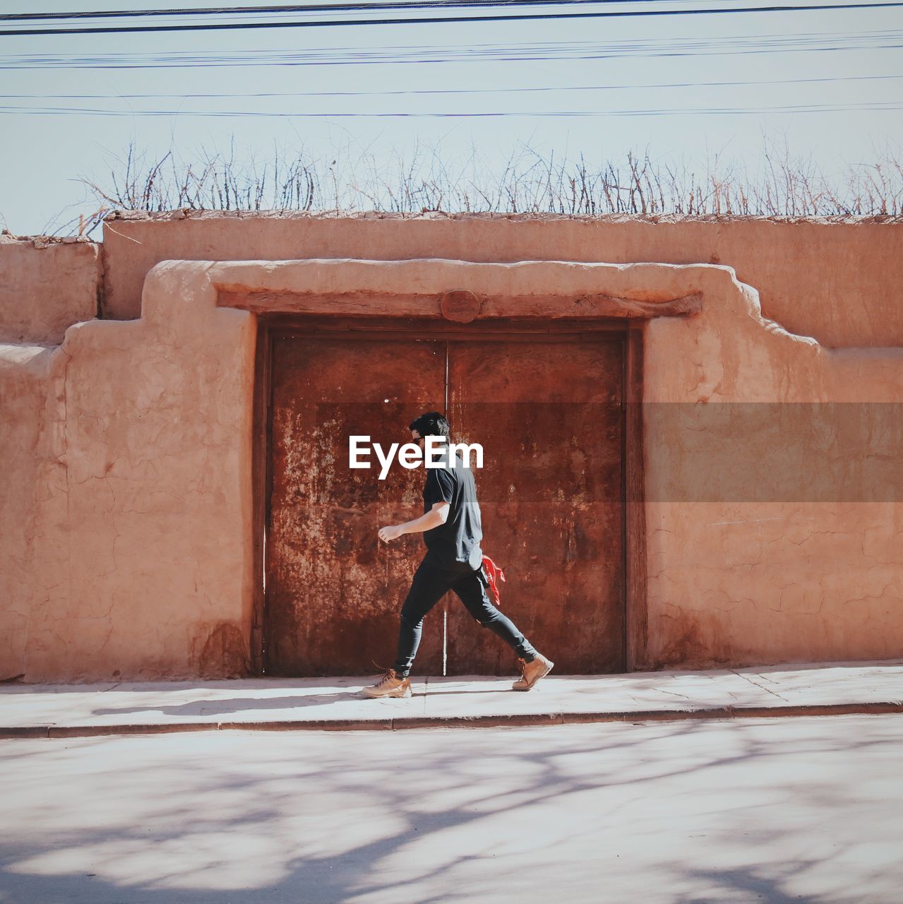 Full length of man walking by doorway on sidewalk during sunny day