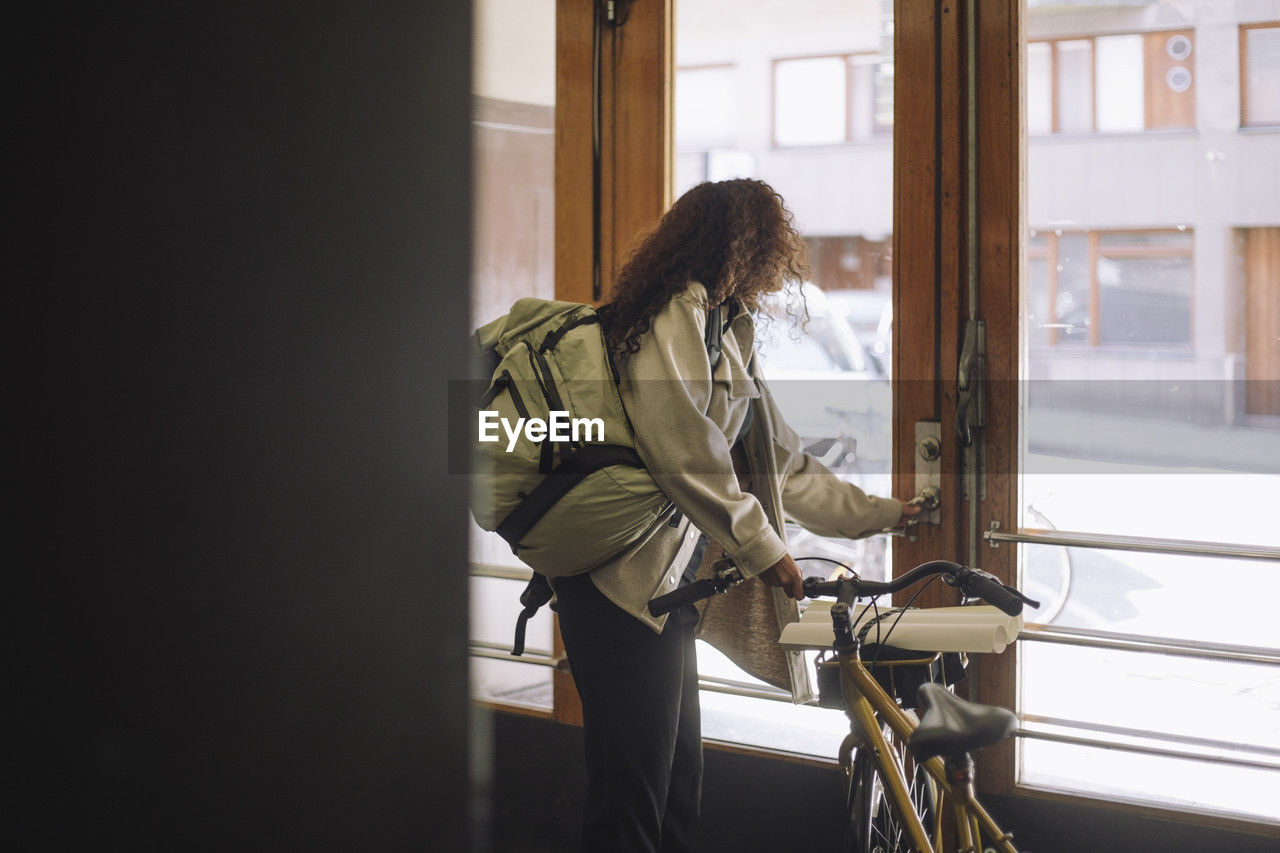 Side view of female freelancer opening door while leaving from building with bicycle