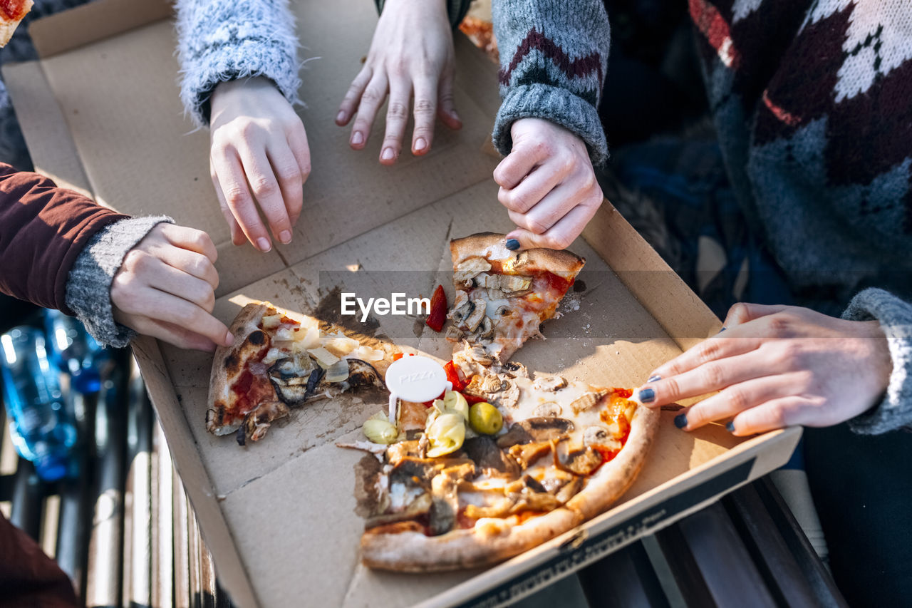 Four friends eating pizza outdoors, partial view