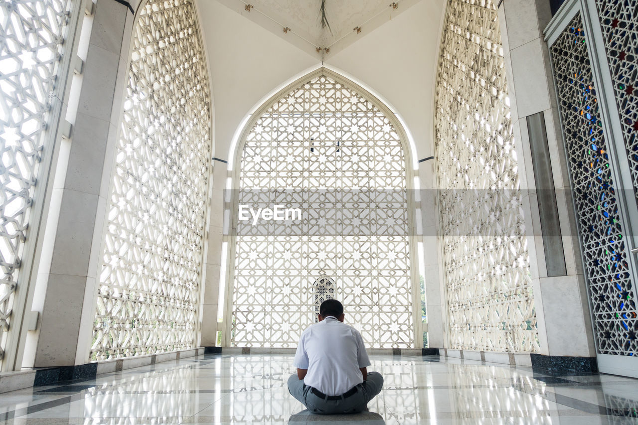 REAR VIEW OF MAN SITTING ON FLOOR IN CORRIDOR