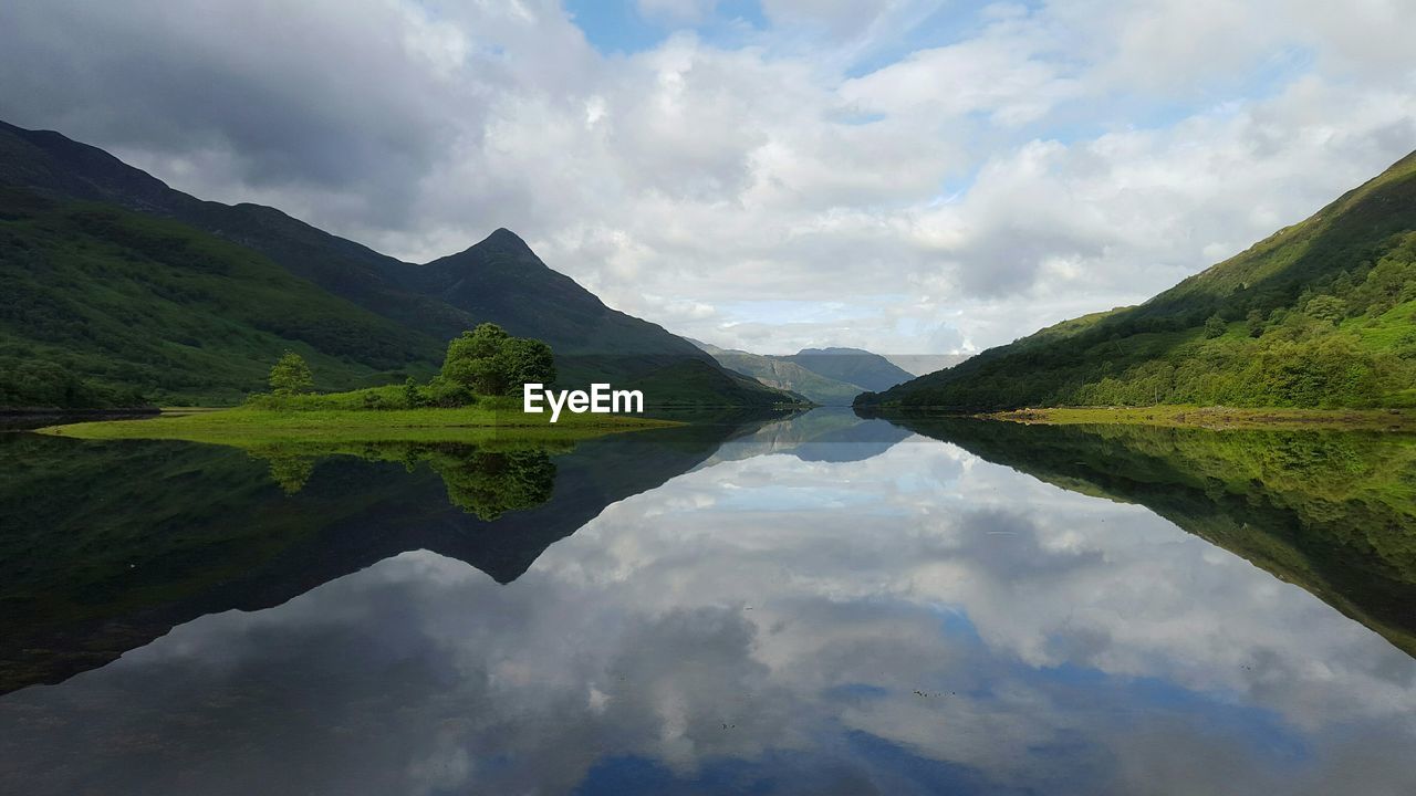 Symmetrical view of mountains and clouds reflecting in lake