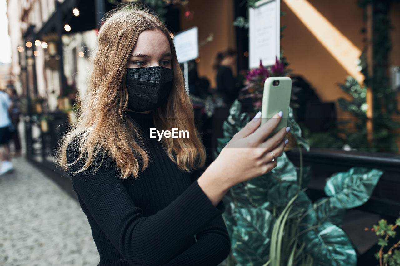 Young woman having video call talking while walking downtown wearing the face mask