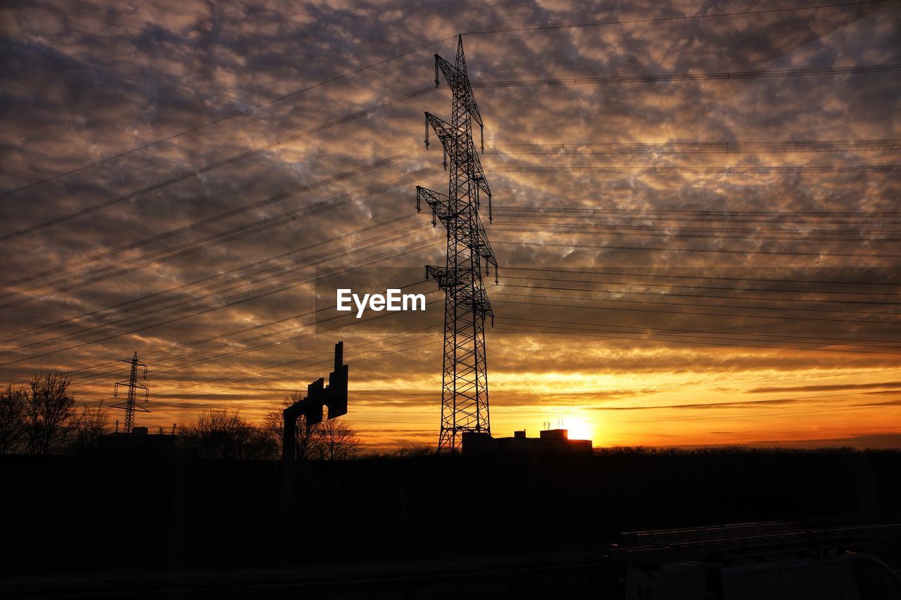 Silhouette electricity pylon on field against sky at sunset