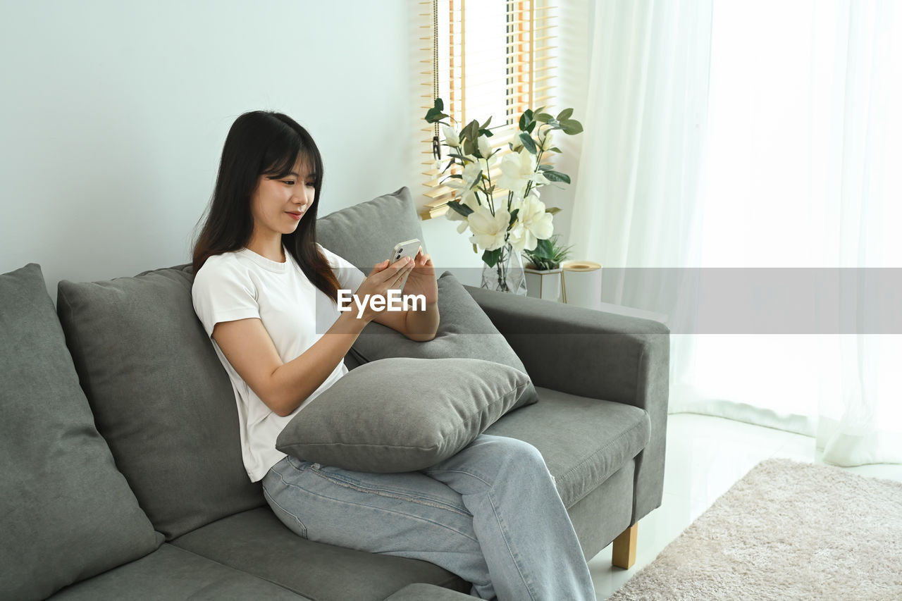 young woman using laptop while sitting on sofa at home