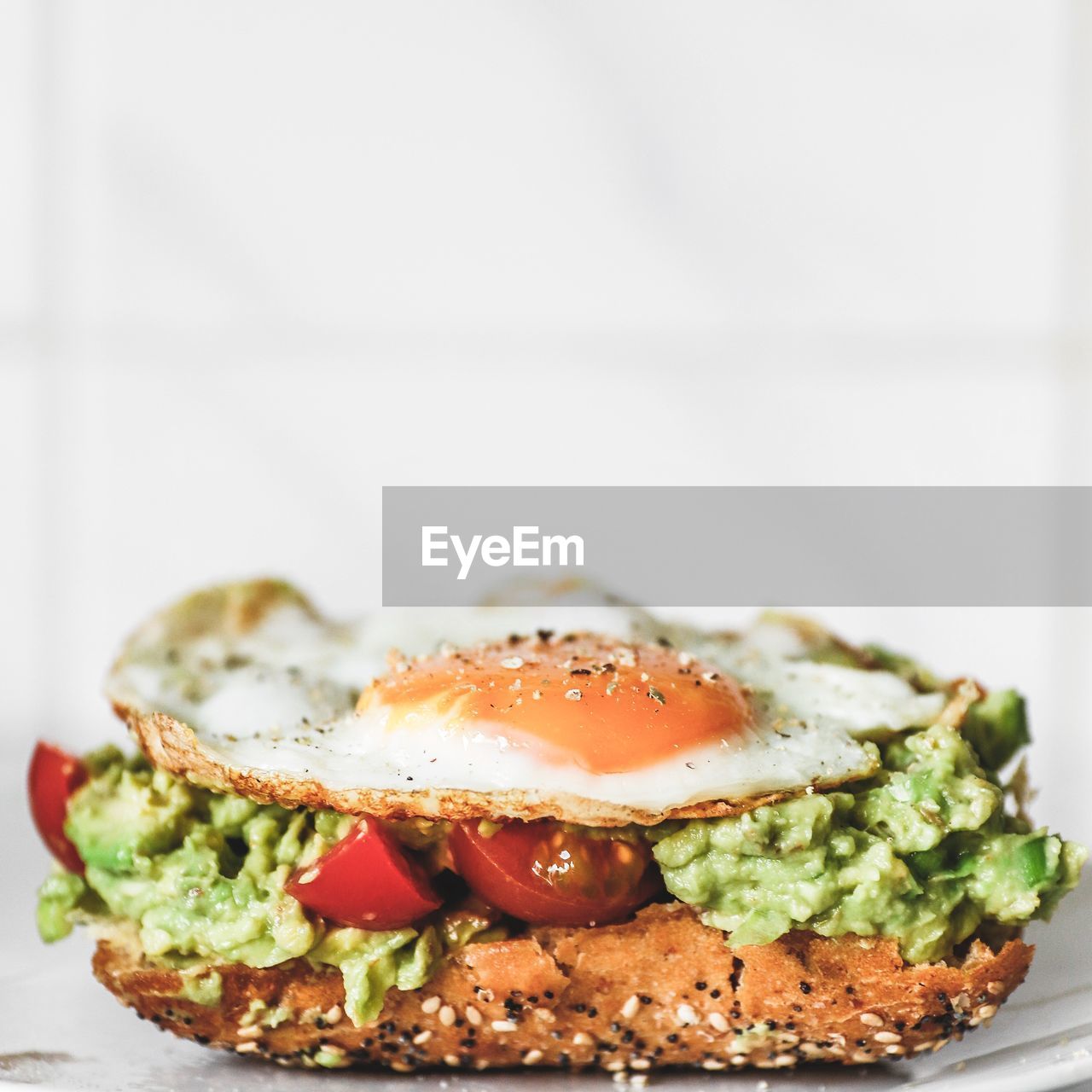 Close-up of fresh breakfast sandwich woth avocado tomato guacamole fried egg served in plate