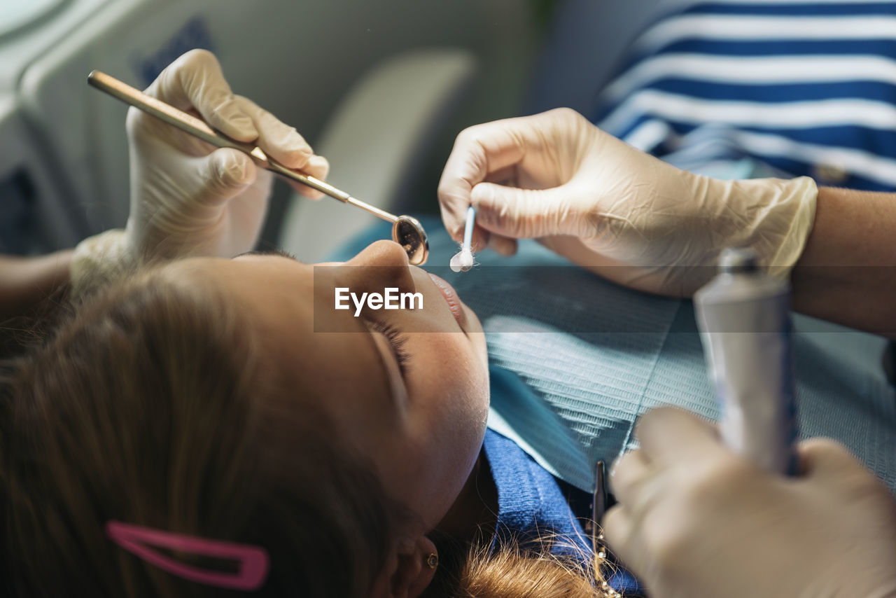 Cropped hands of dentists examining girl at clinic