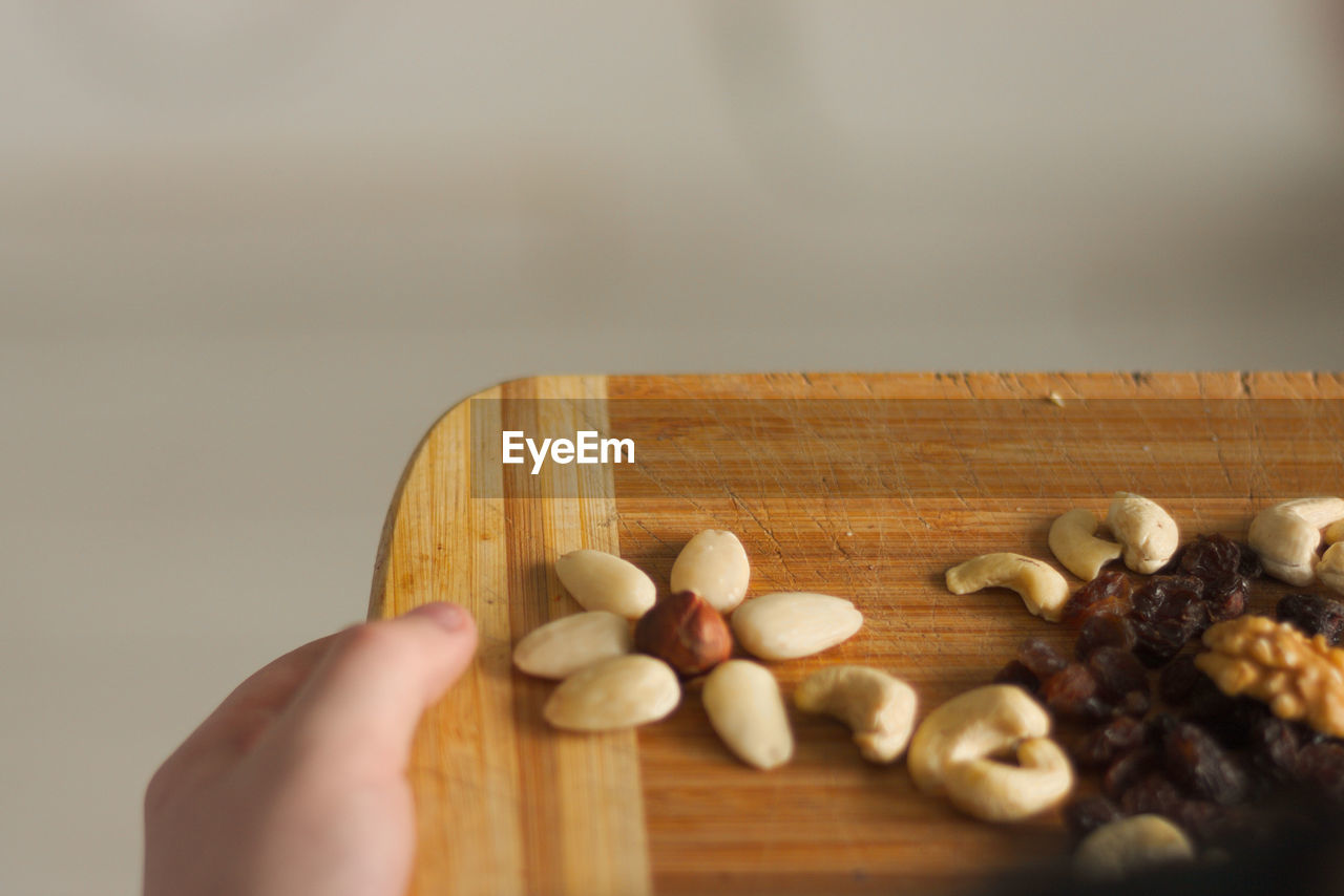 Cropped image of person holding nuts on cutting board