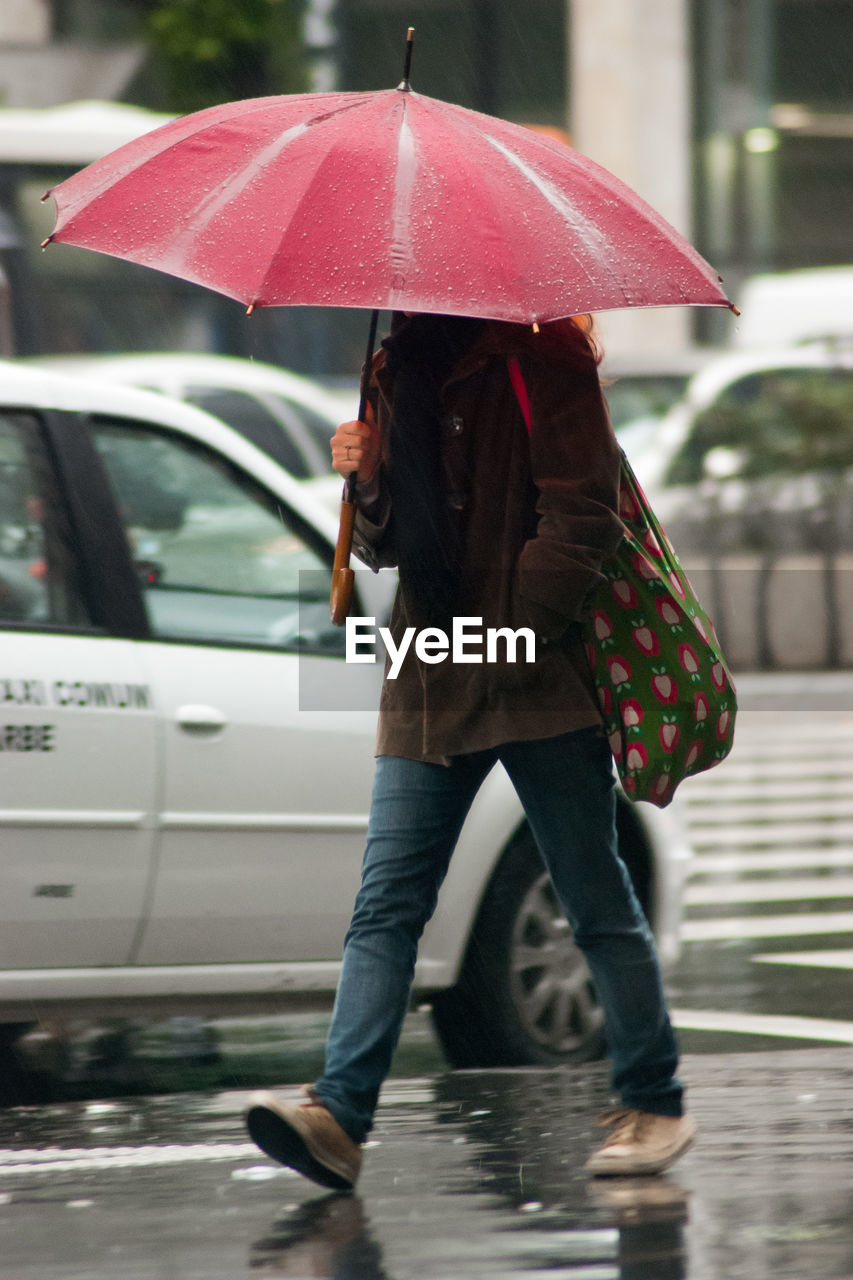 Woman with umbrella walking on wet street during rainy season