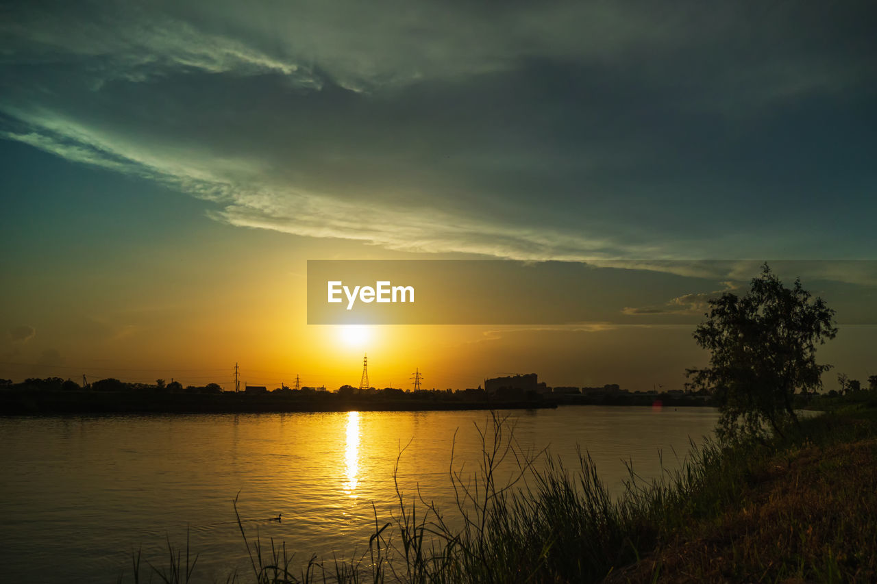 sky, water, beauty in nature, sunset, cloud, tranquility, scenics - nature, nature, tranquil scene, reflection, lake, plant, environment, afterglow, dawn, landscape, no people, sun, evening, idyllic, tree, horizon, sunlight, silhouette, outdoors, dramatic sky, orange color, non-urban scene, land, grass, beach, atmospheric mood, travel destinations