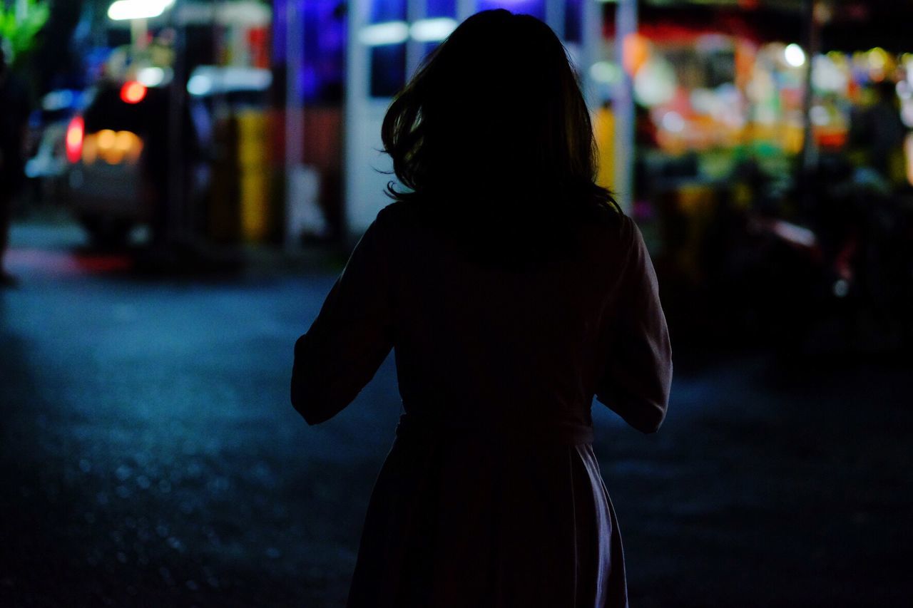 Rear view of woman standing on street at night