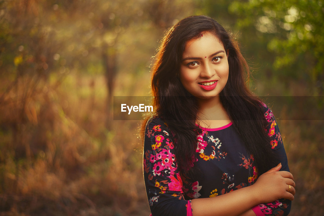 Portrait of young woman standing against trees