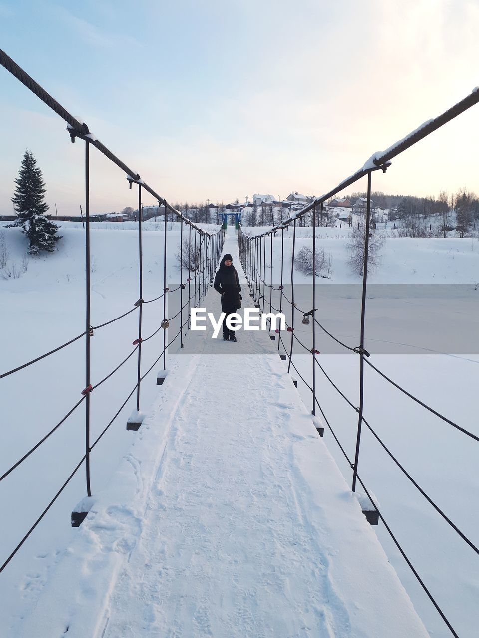 Portrait of young woman standing on snow covered footbridge against sky