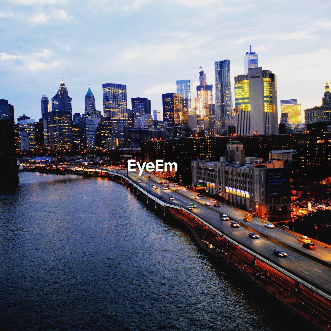 Illuminated buildings by river against sky in new york city.