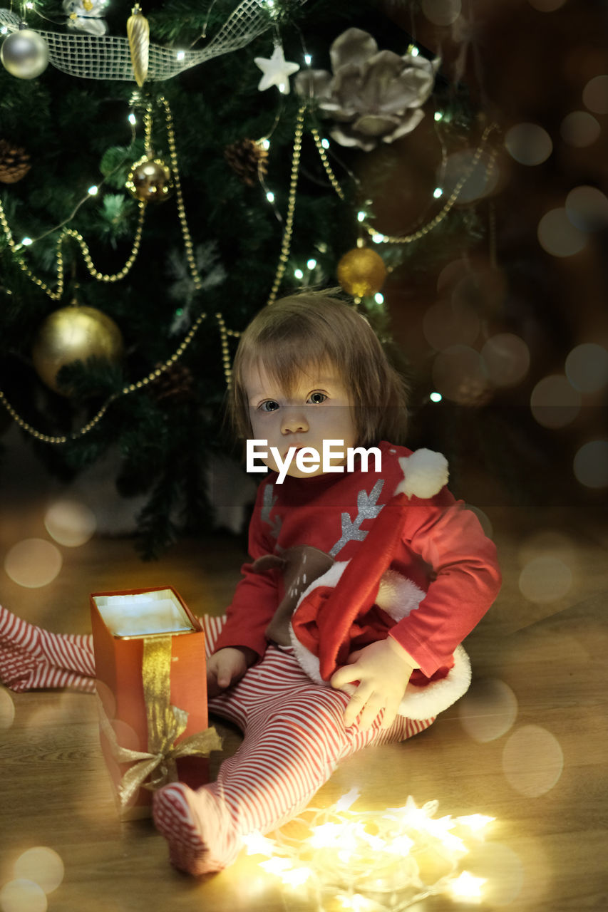 Portrait of cute girl sitting by christmas tree