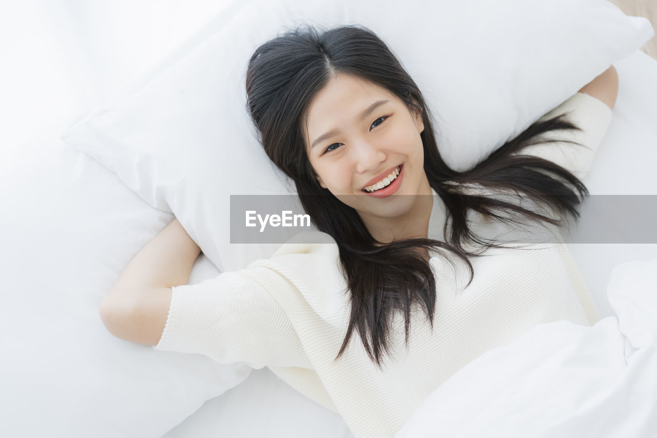 Portrait of smiling young woman relaxing on bed at home