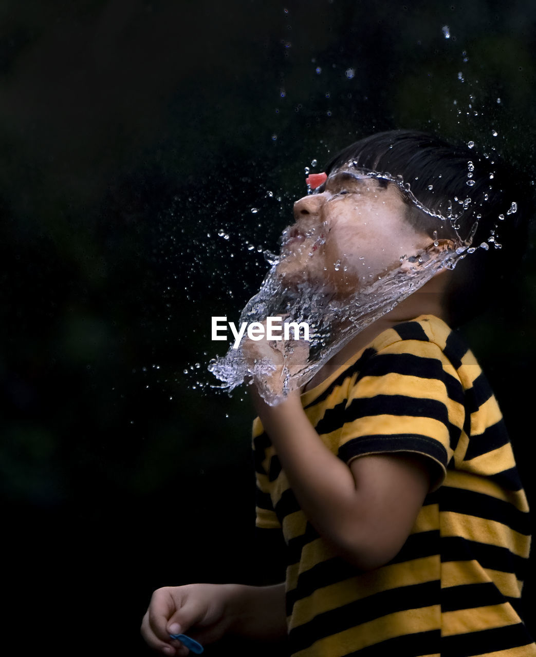 Playful boy with water splashing on his face against black background