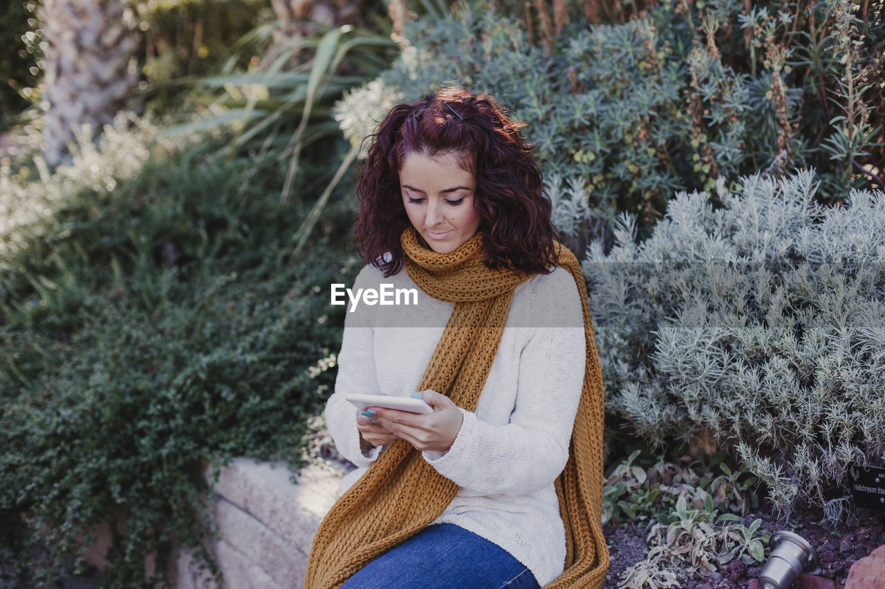 Woman using digital tablet while sitting against plants