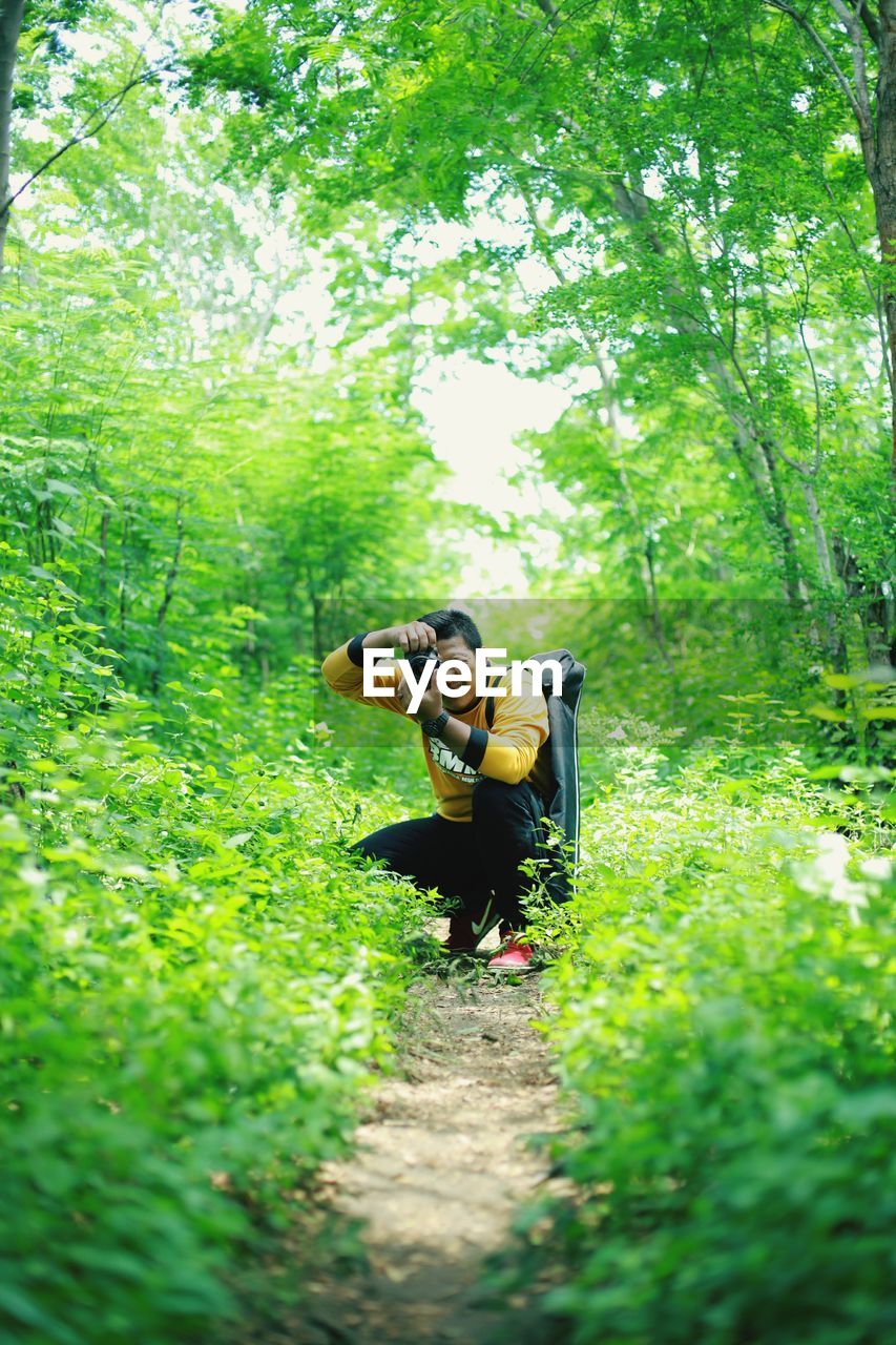 Man photographing while crouching in forest