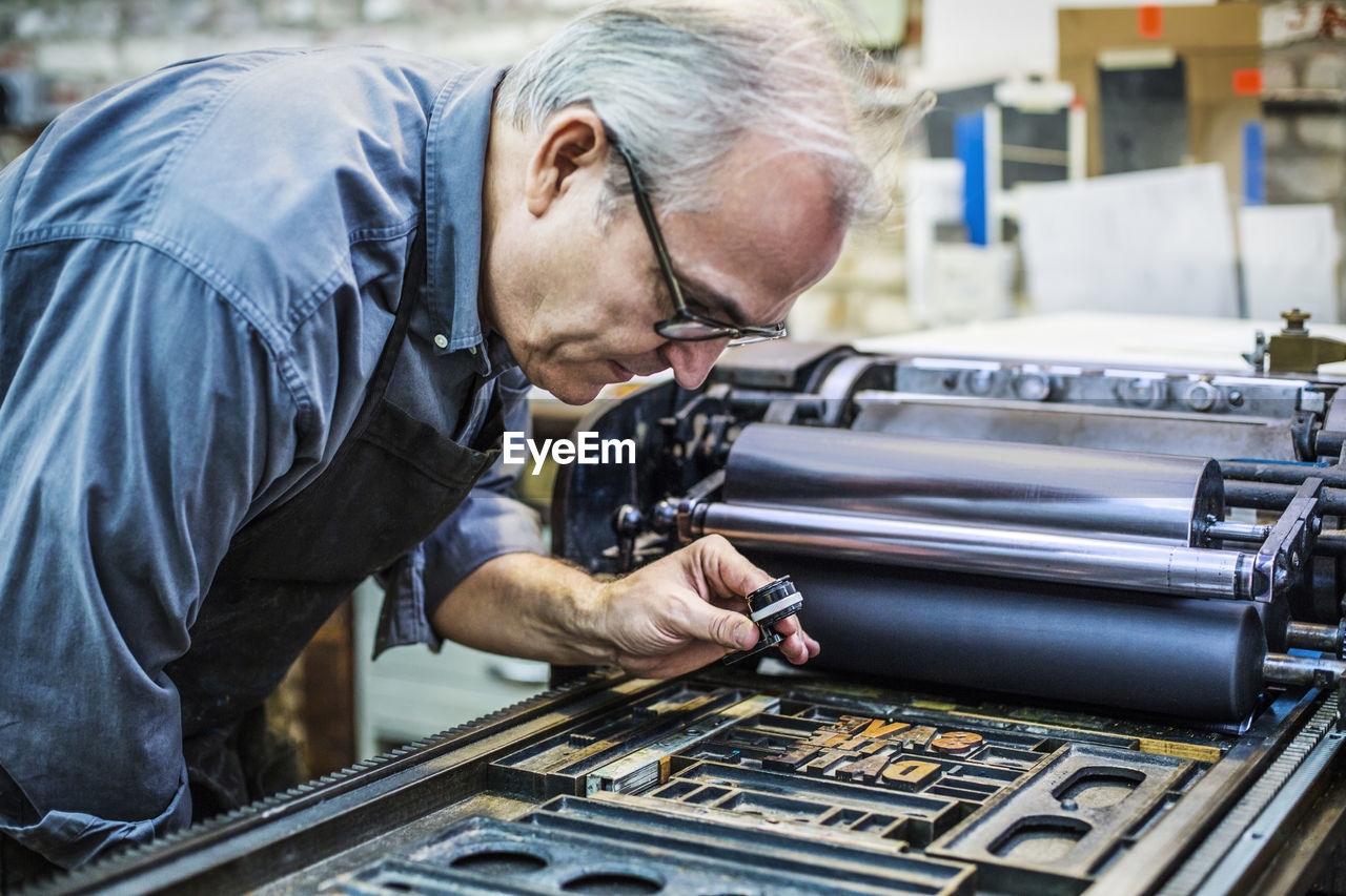 Side view of senior man examining letterpress through magnifying glass at workshop