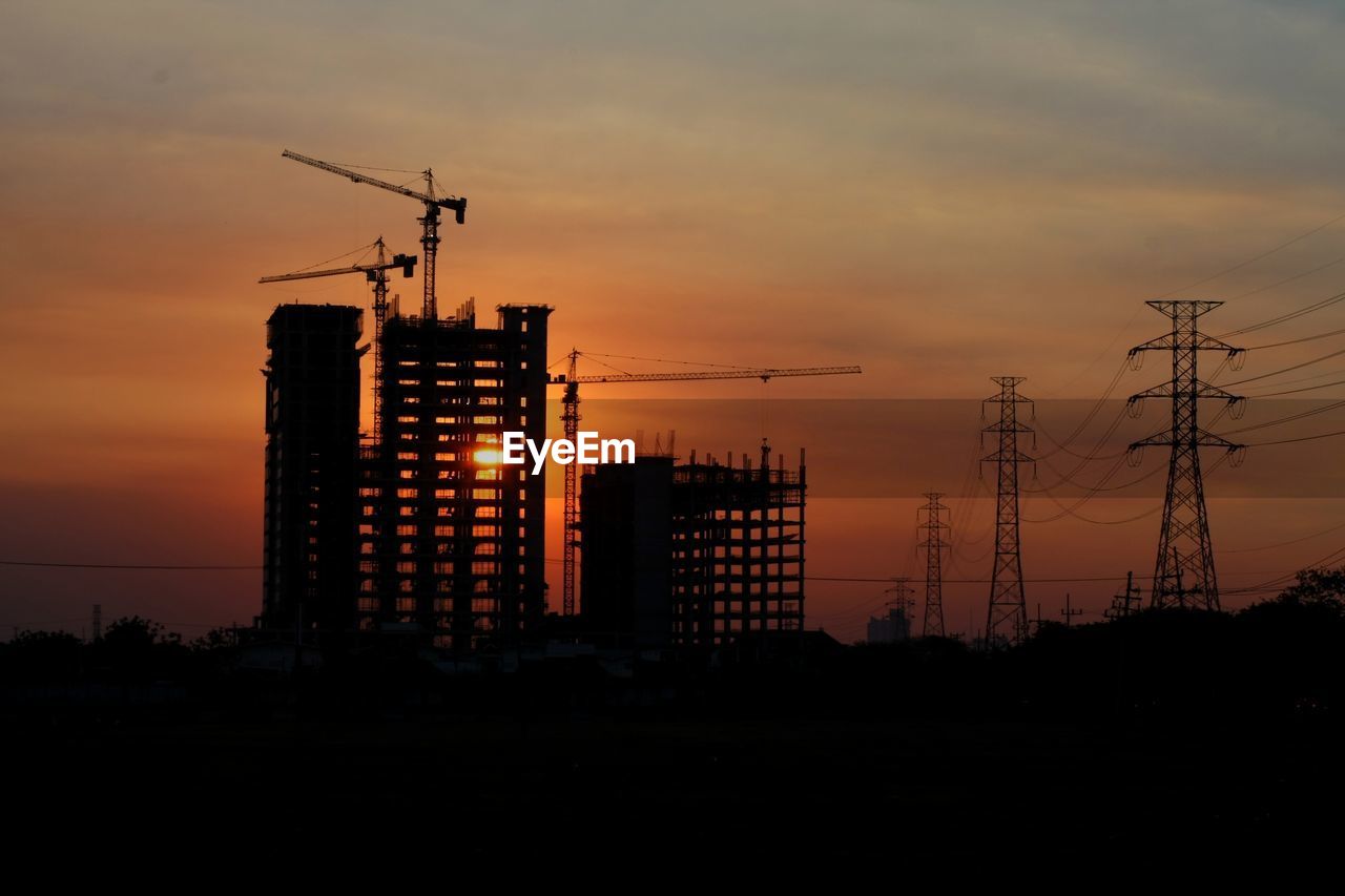 Silhouette cranes at construction site during sunset