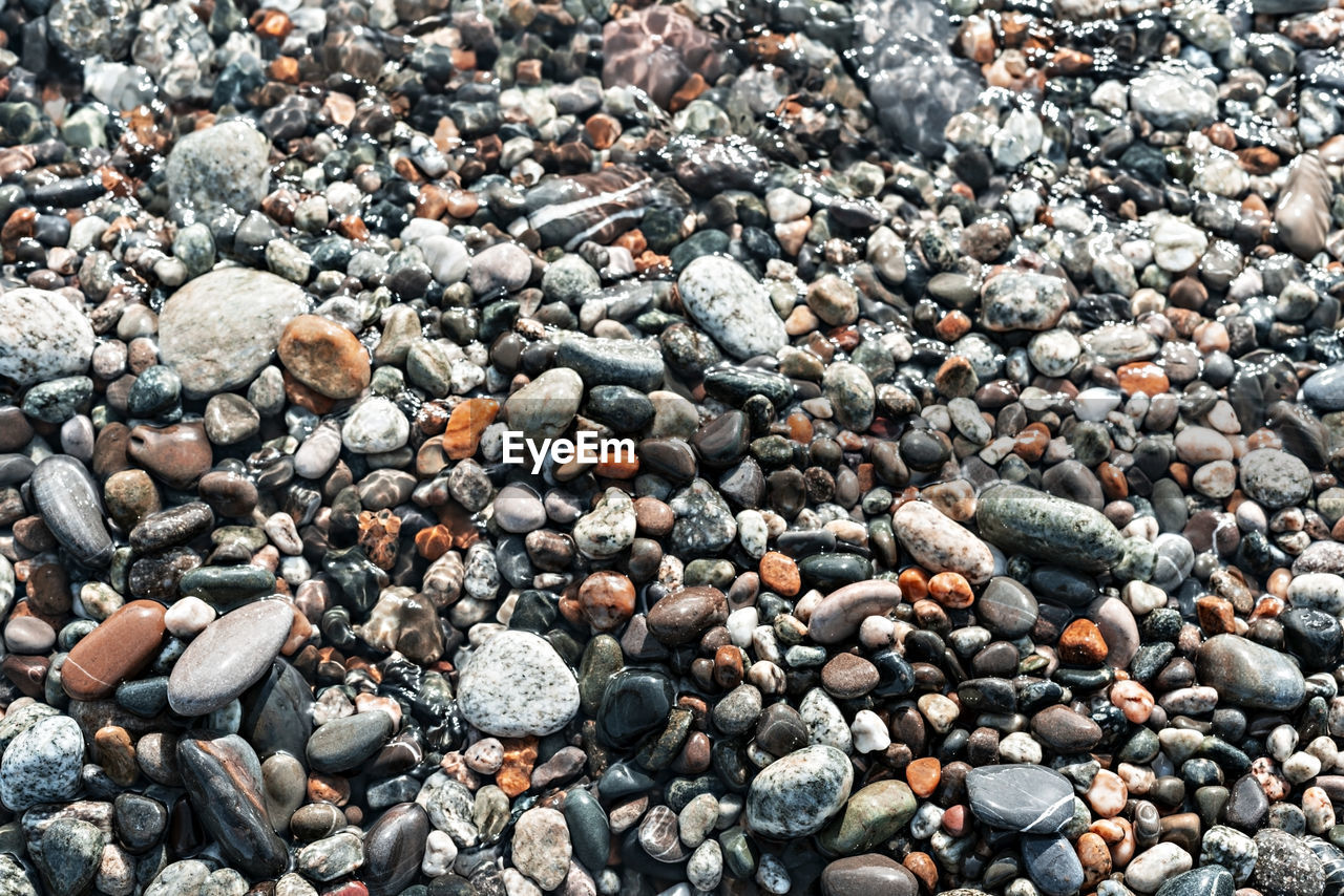 Pebble shore close up, natural background copy space, gray and red pebbles in sea water, texture