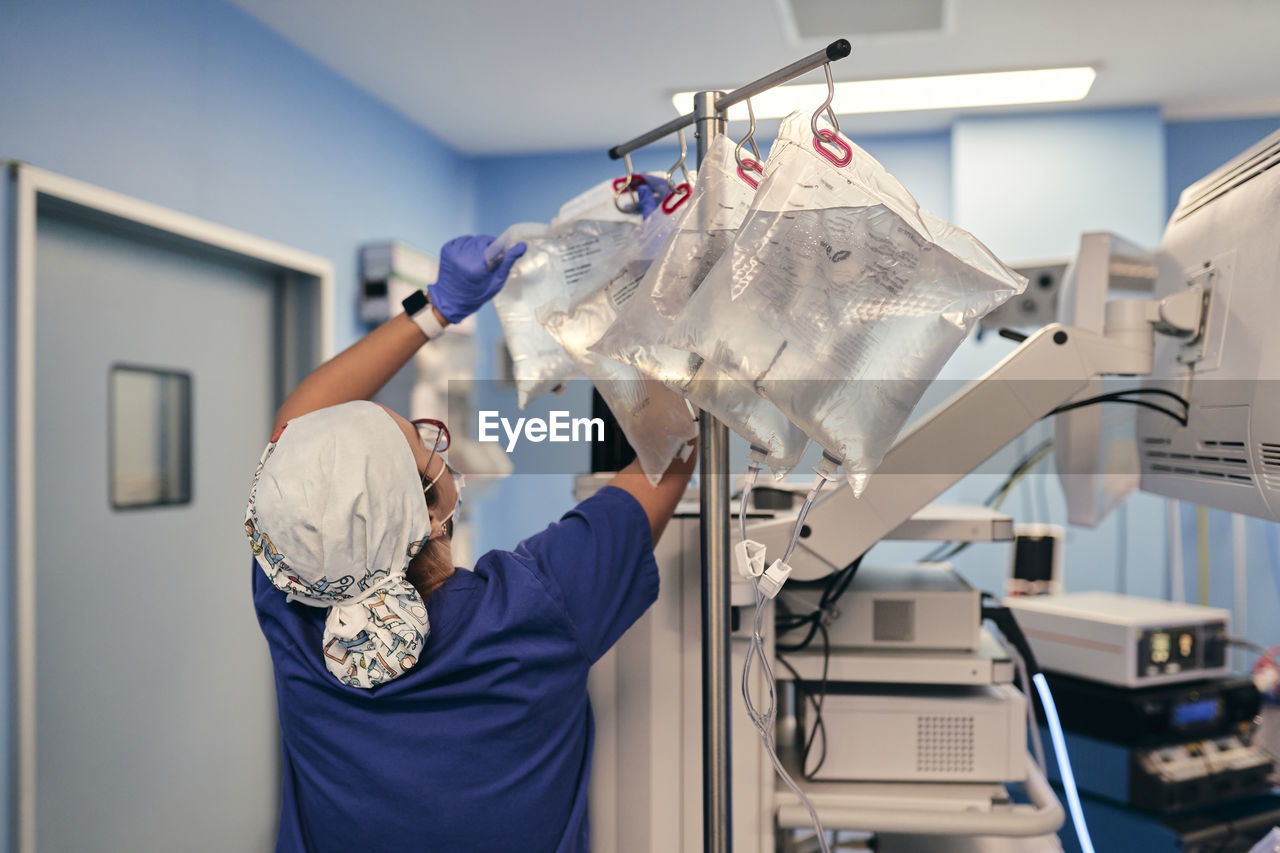 Male doctor removing iv drip bag while standing by monitoring machine in operating room