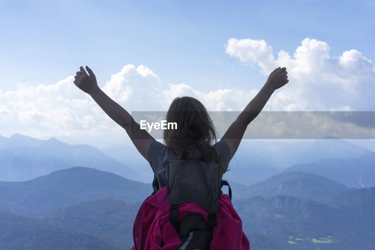 Rear view of female hiker with arms raised against sky at mountain