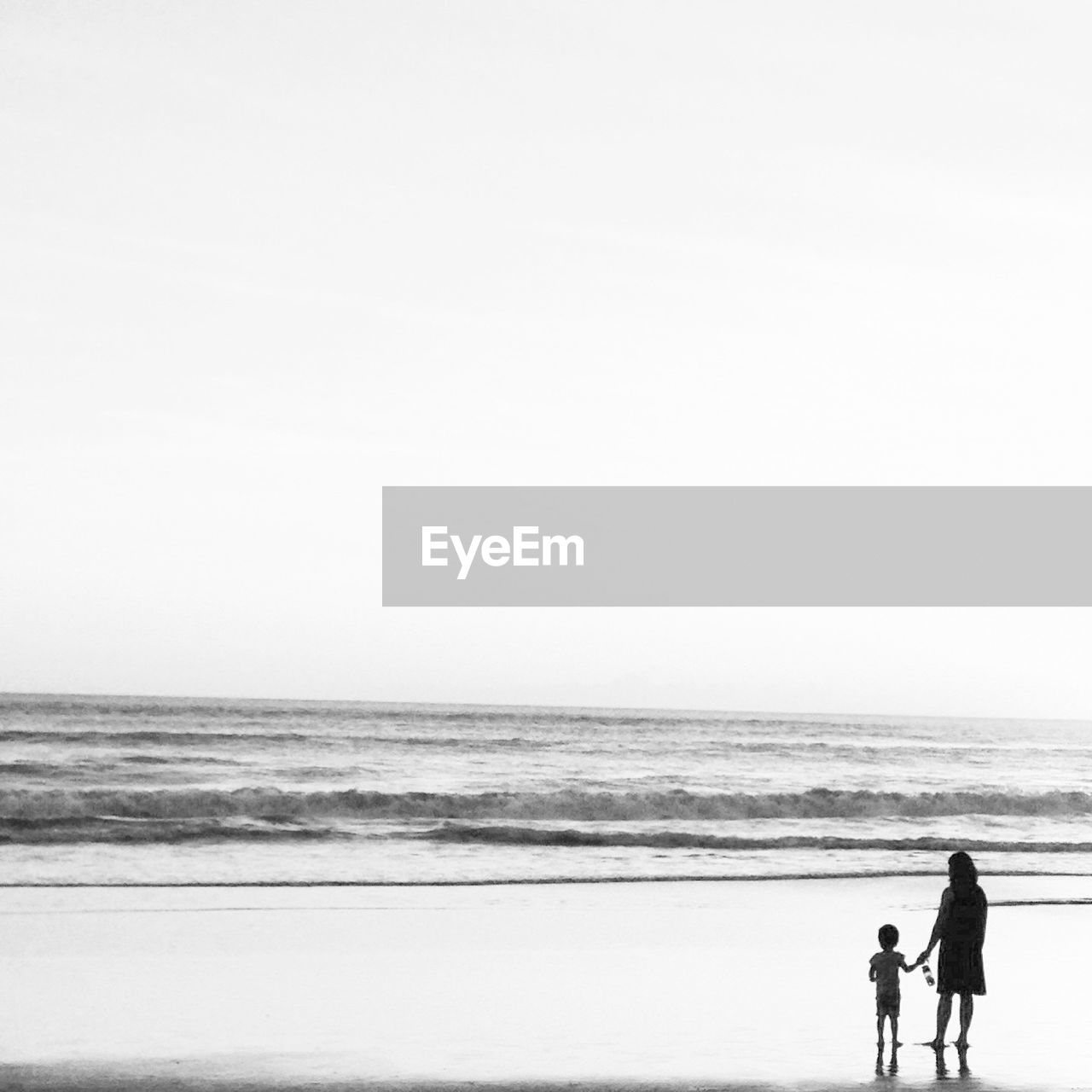 Mother and son walking on beach against clear sky