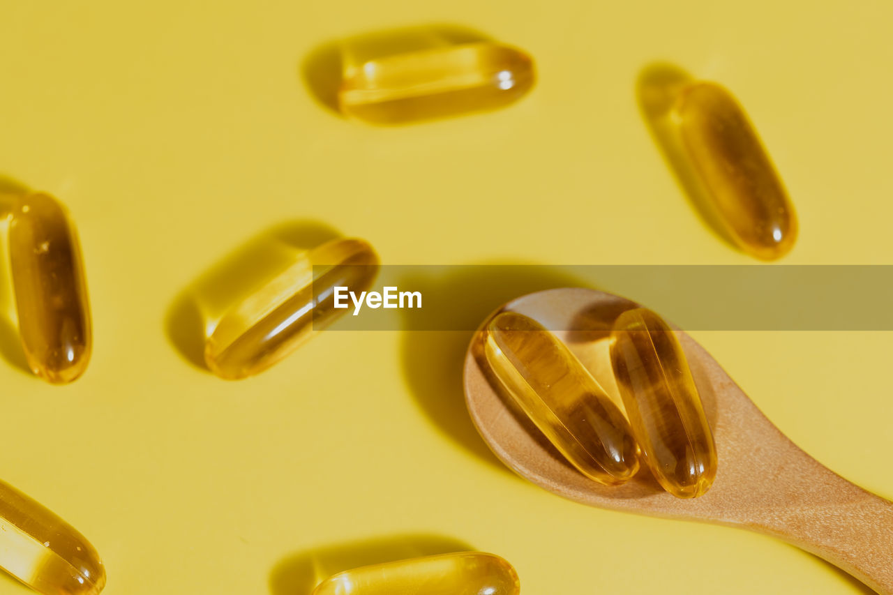 Omega-3 fish oil capsules in the wooden spoon on yellow background for healthcare concept