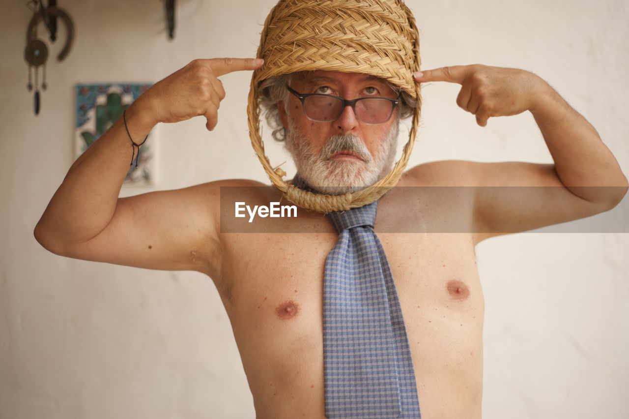 Senior man with basket on head standing against wall at home