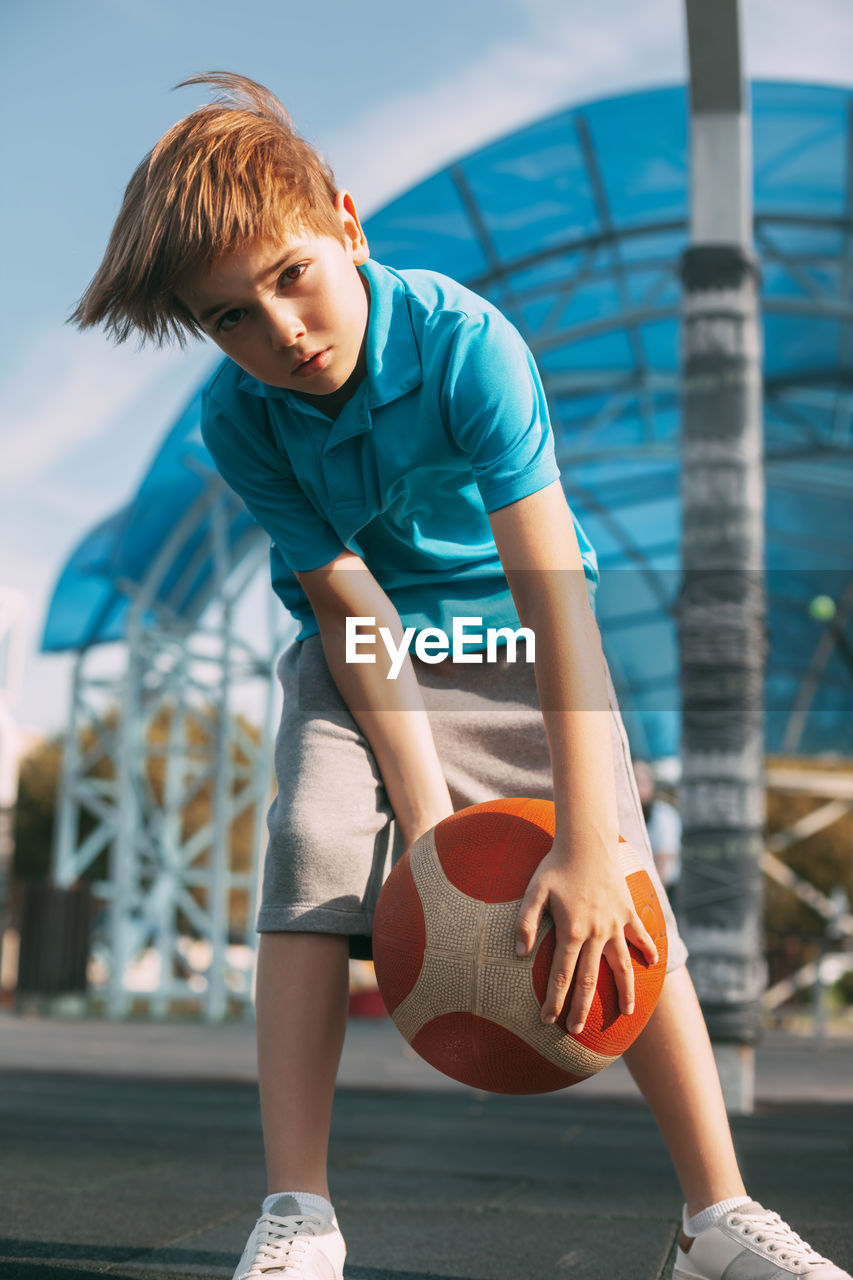 A beautiful boy in a sports uniform caught a basketball. a boy holds a ball in his hands 