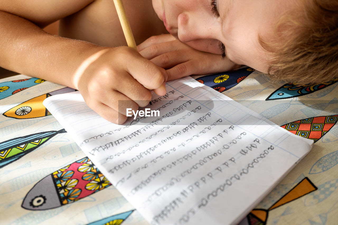 High angle view of cute boy writing in book on table