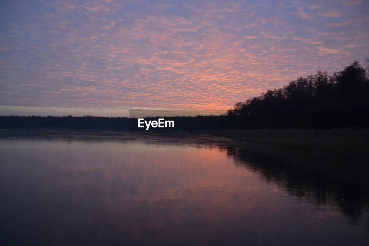 REFLECTION OF SILHOUETTE TREES ON LAKE AGAINST SKY