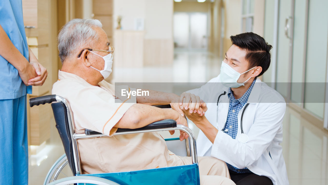 Smiling doctor wearing flu mask consoling patient in hospital