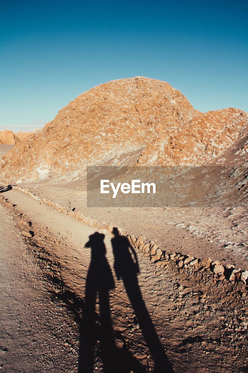 Shadow of two people on desert against clear sky