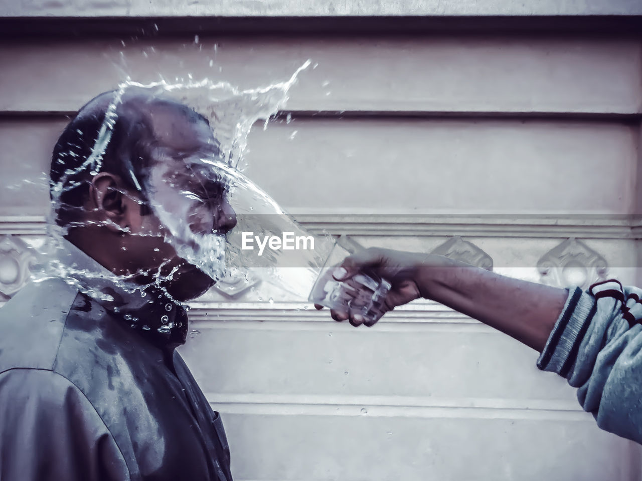 Cropped image of hand splashing water on man against wall