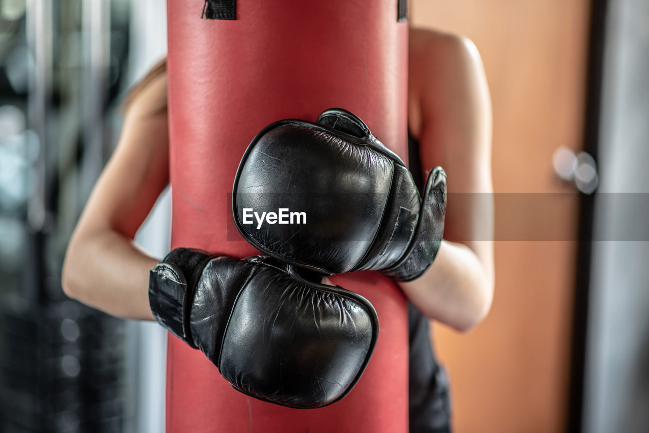 Midsection of woman embracing punching bag in gym