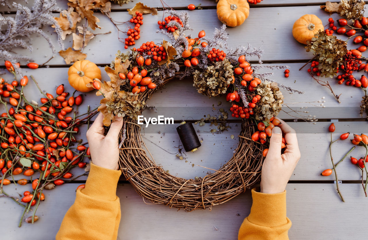 Girl making floral autumn door wreath using colorful rosehip berries, rowan, dry flowers and pumpkin