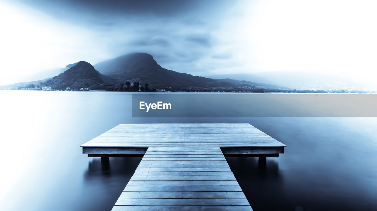 Jetty on pier by lake against sky