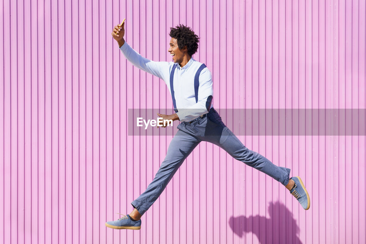 Full length of man with arms raised standing against pink wall