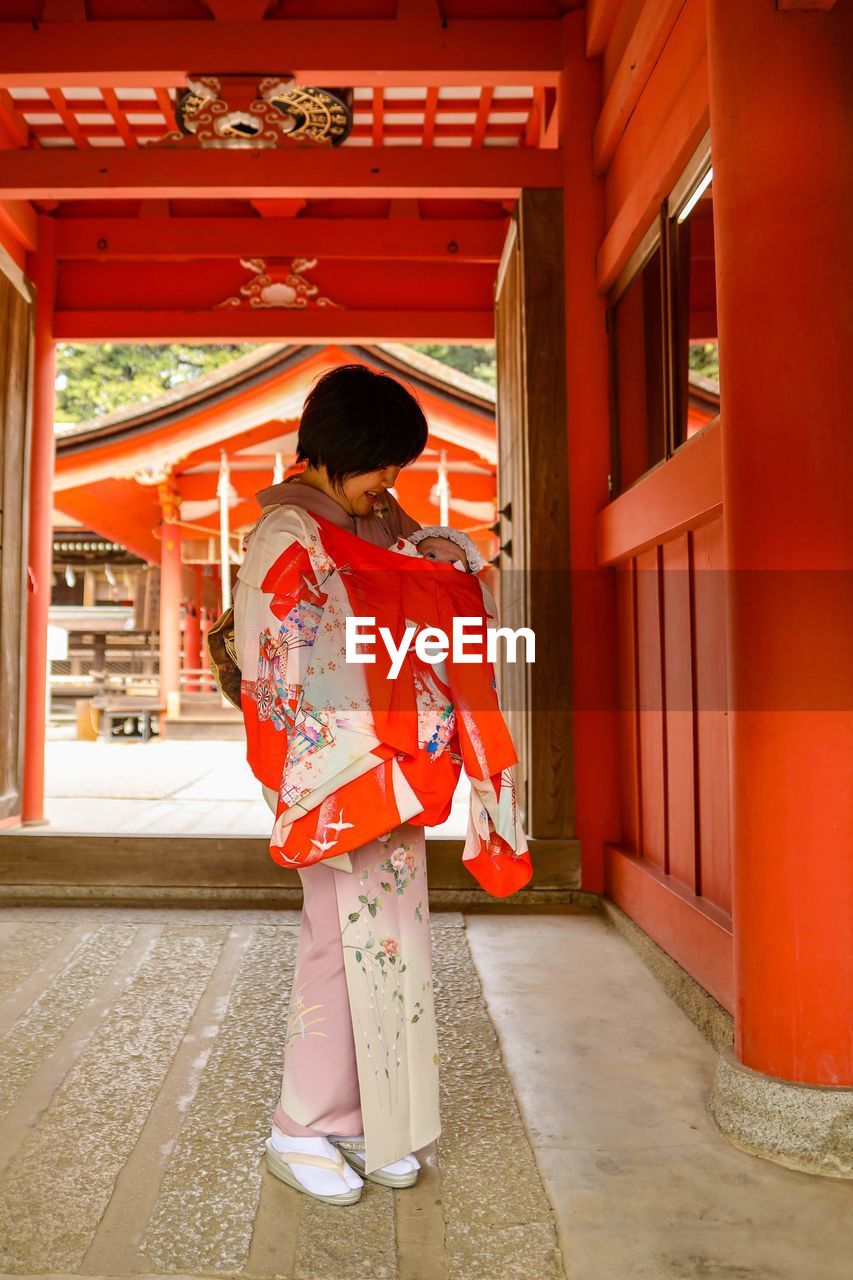 Full length of woman wearing kimono standing with baby girl in temple