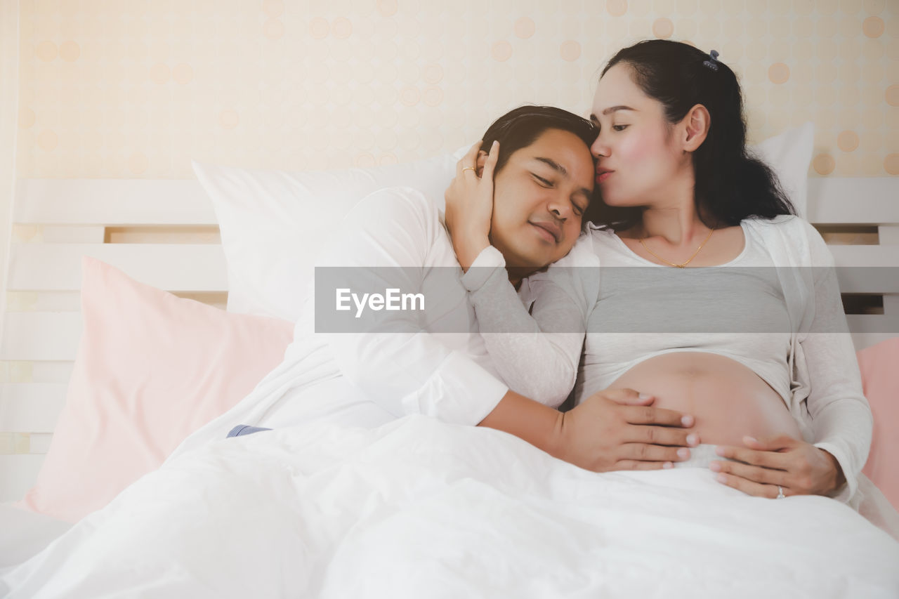 Portrait of smiling couple sitting on bed at home