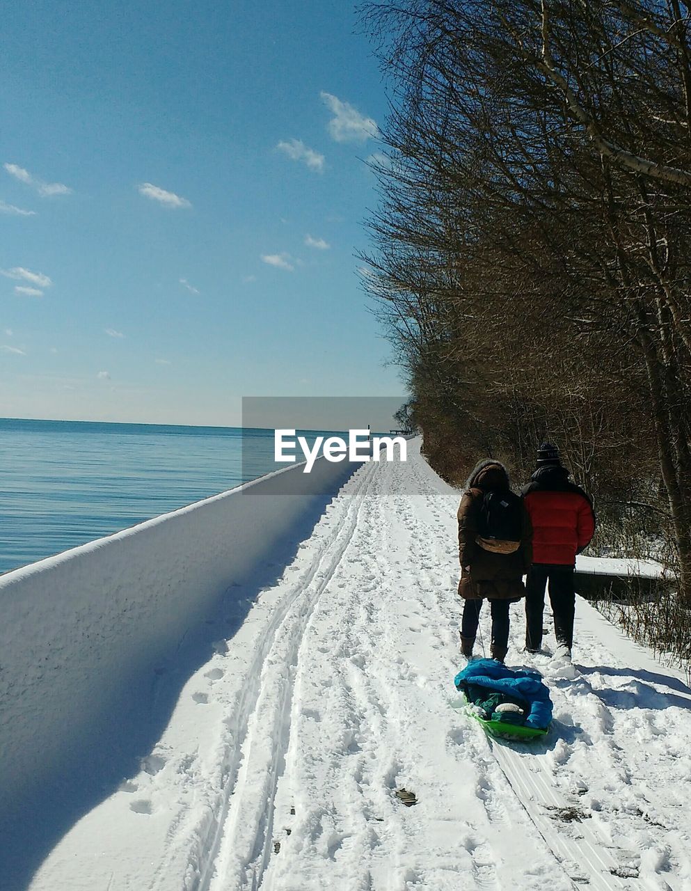 Rear view of people with sled on snow covered lakeshore