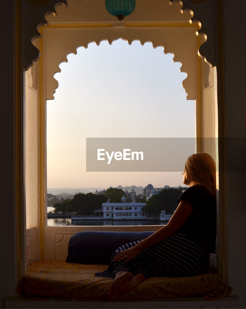 Full length of thoughtful young woman looking through window