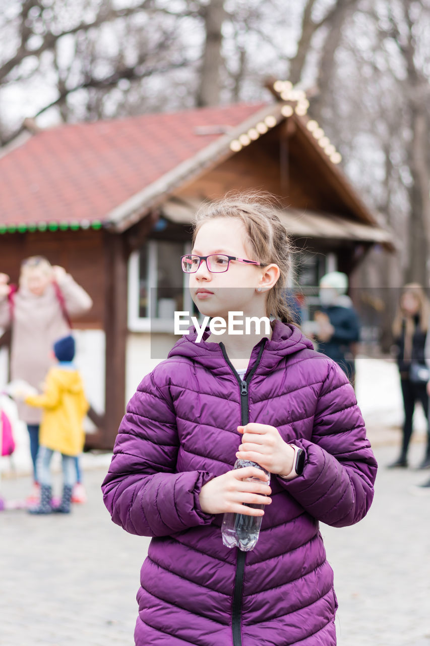 A cute girl in glasses holds a bottle with water bought in a food truck in a city park