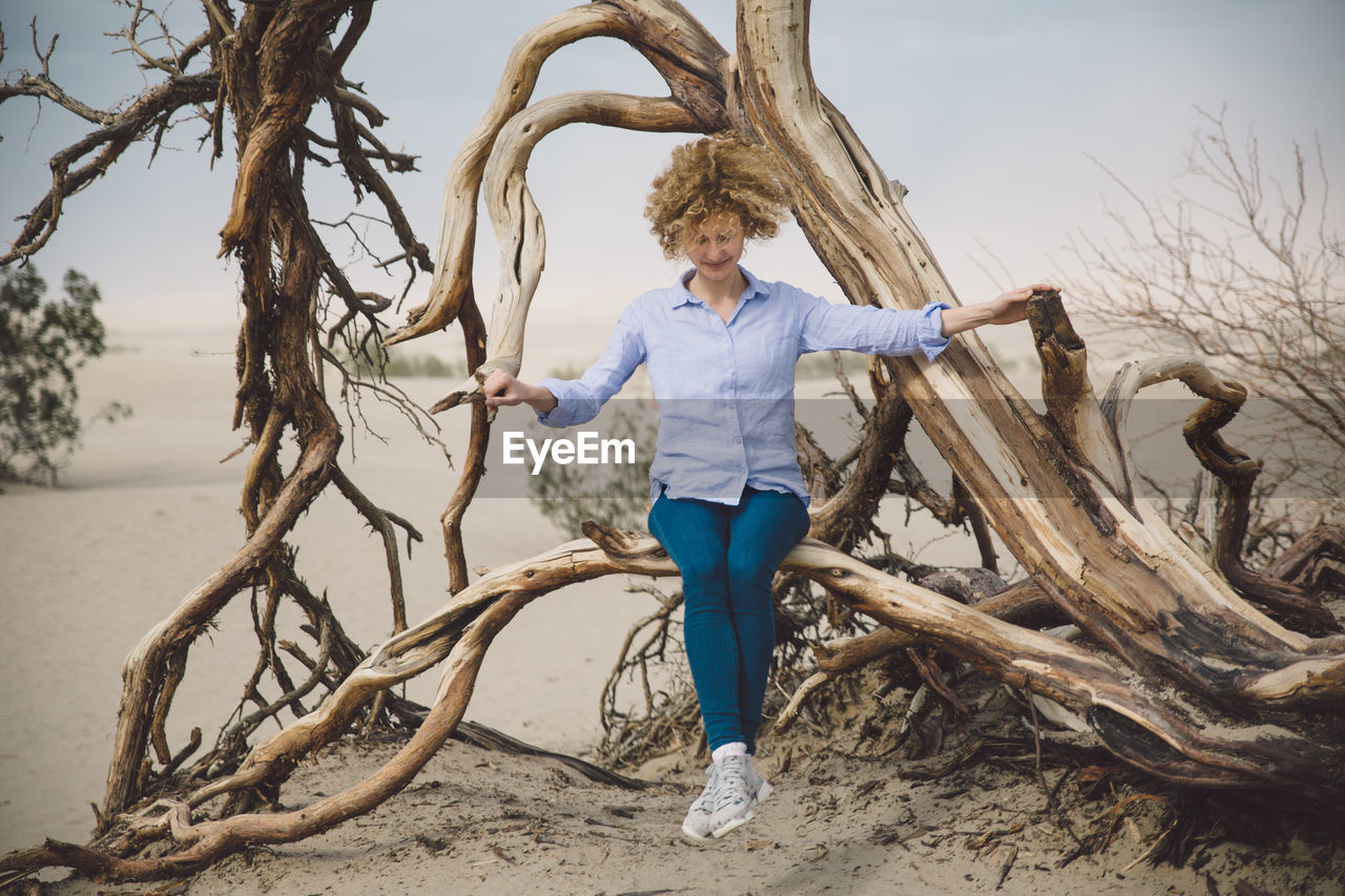 Full length of young woman sitting on tree