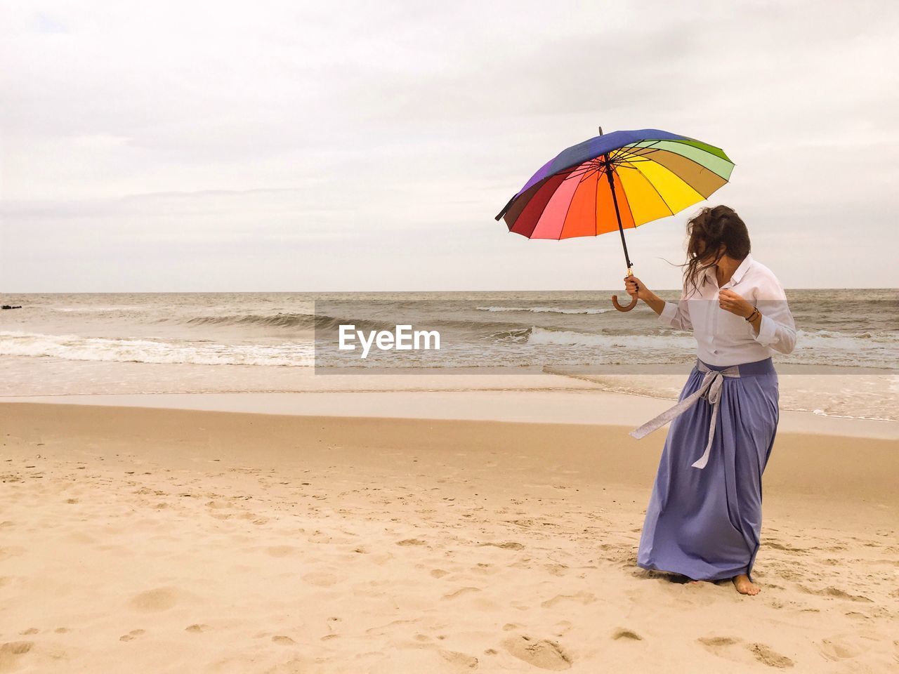 Young woman standing with umbrella on beach against sky